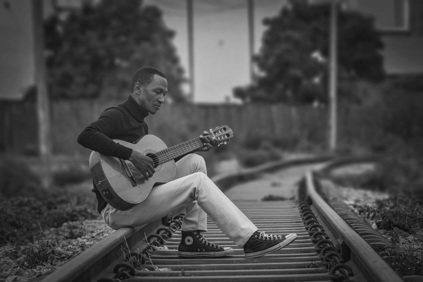 a man sitting on a train track playing a guitar