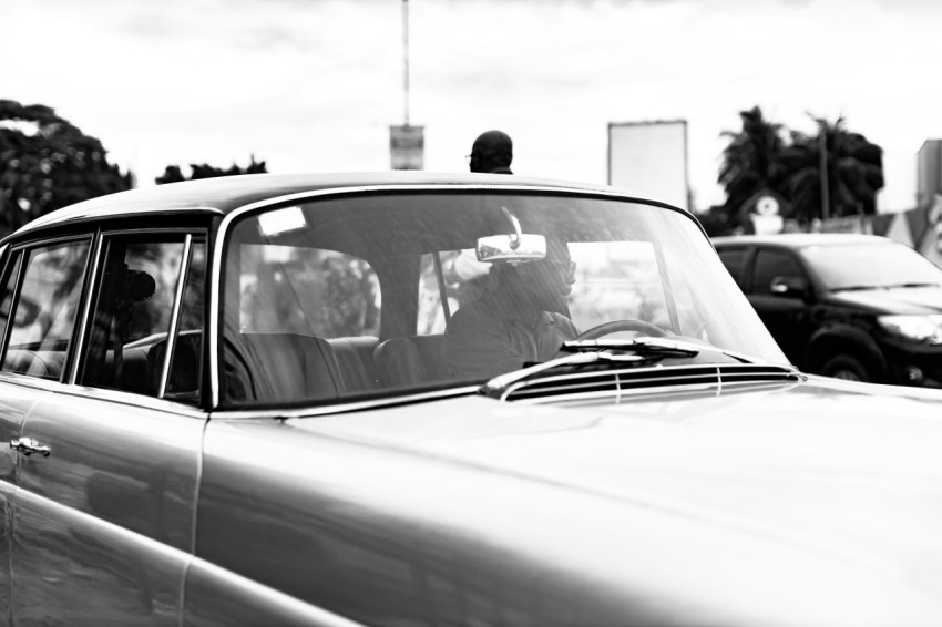 a black and white photo of a man driving a car w