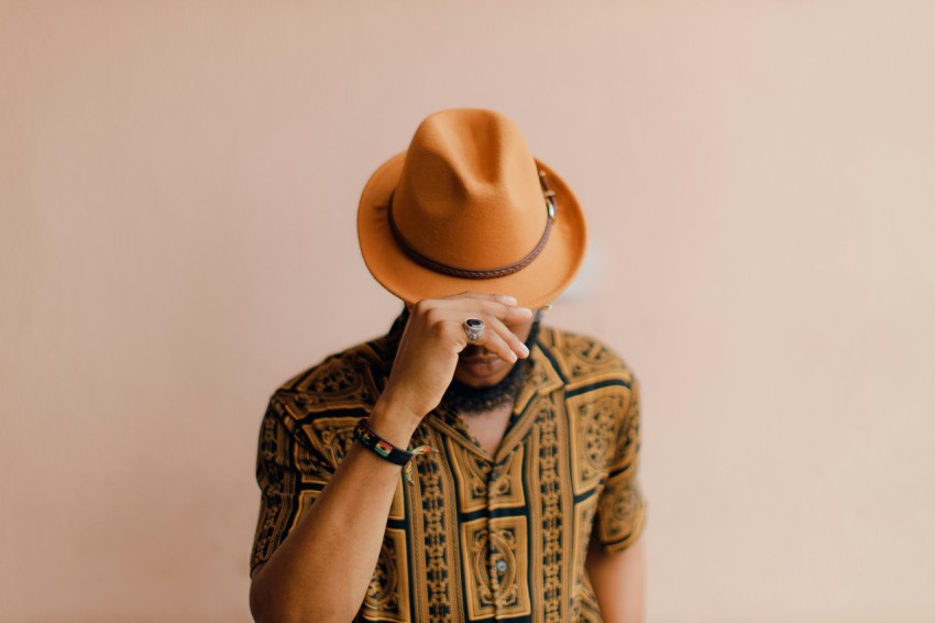 a man wearing a brown hat while holding his hand to his face