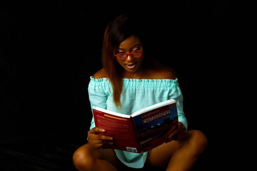 woman in blue off shoulder shirt holding red and white book