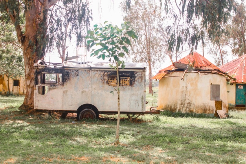 an old trailer parked in a field next to a tree l2G