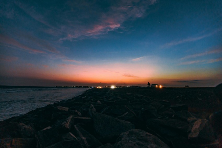 the sun is setting over the ocean with rocks in the foreground