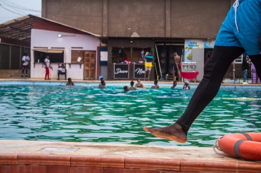 a person standing on a ledge above a pool with people in the background