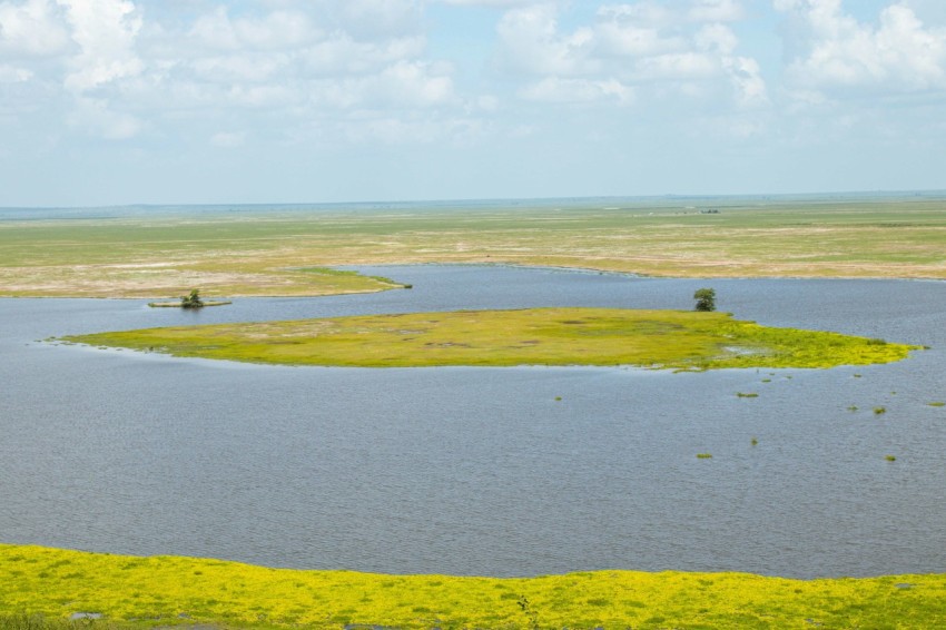 a large body of water surrounded by a lush green field FsHJn