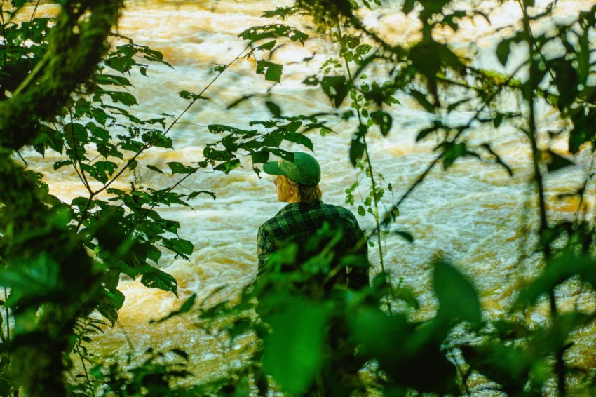 a man standing in front of a river surrounded by trees zM0Gb