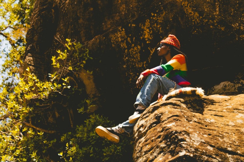 a man sitting on top of a large rock next to a forest