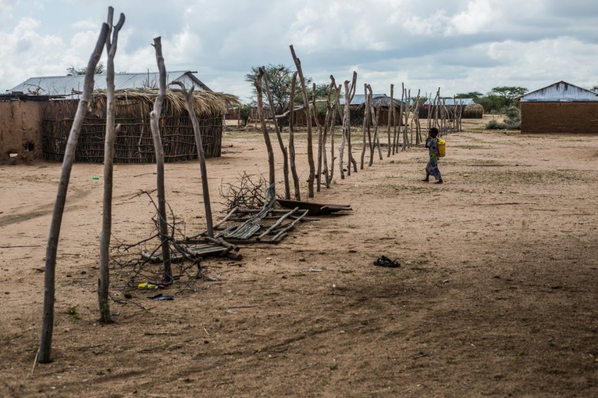 a small child standing in a dirt field next to a fence