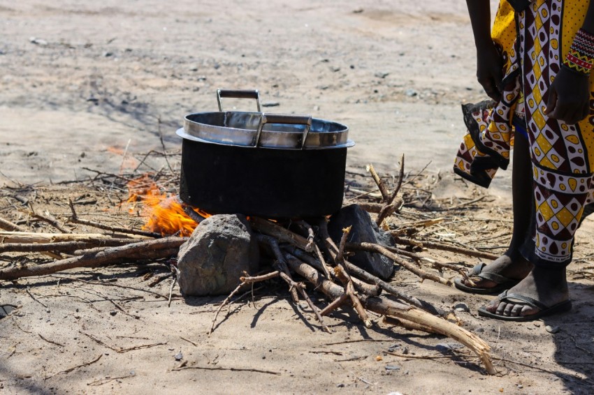 a person standing next to a fire with a pot on top of it