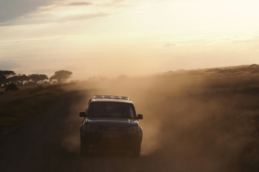 a car driving down a dirt road in the middle of a field