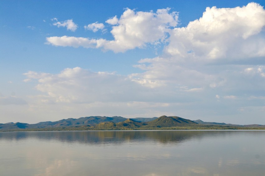 body of water near mountain under blue sky and white clouds during daytime