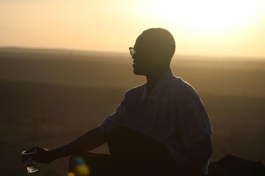 a man sitting on top of a hill with a wine glass in his hand