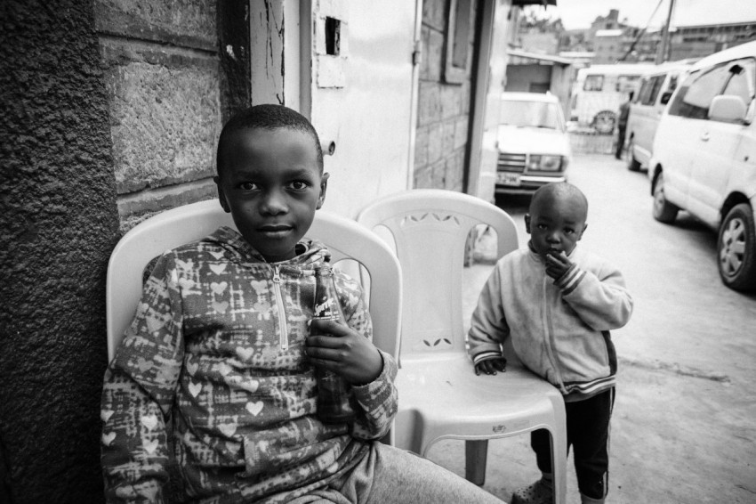 first boy sitting on monobloc chair near second boy who is standing beside monobloc chair