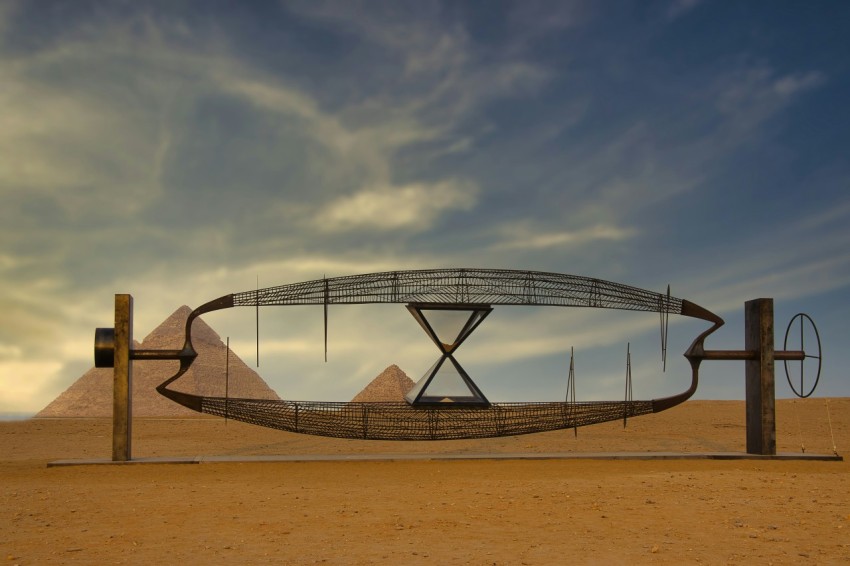 a sculpture in the middle of a desert with pyramids in the background