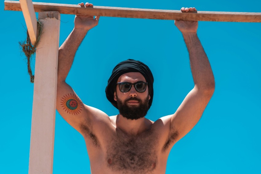 topless man wearing black sunglasses holding on blue metal bar