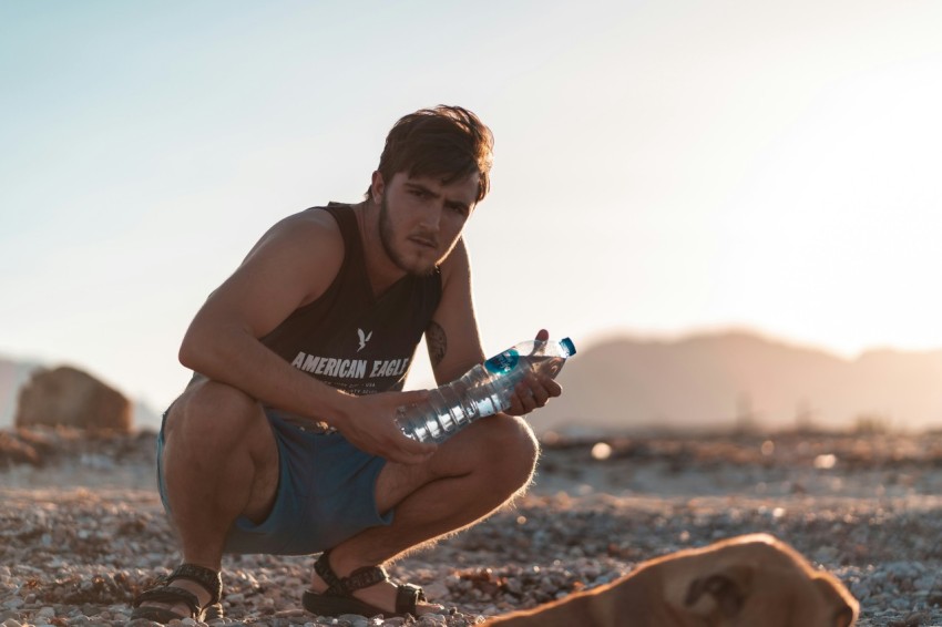 man in black tank top and blue denim shorts sitting on brown sand during daytime 7xc3cvAj