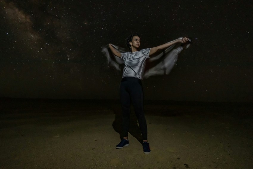 a man standing in the middle of a desert under a night sky filled with stars Hmb7v