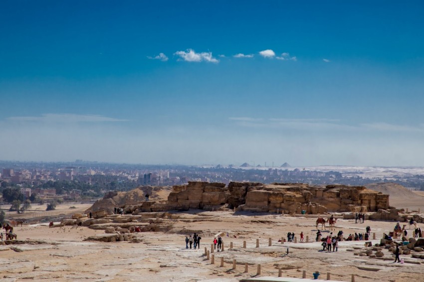 a large group of people on a sandy beach with a large rock formation in the background