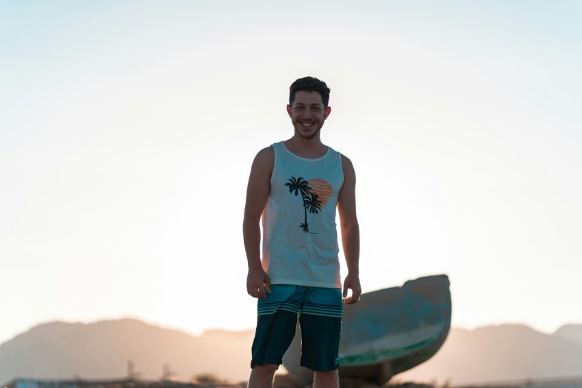 man in white tank top and black shorts holding brown surfboard