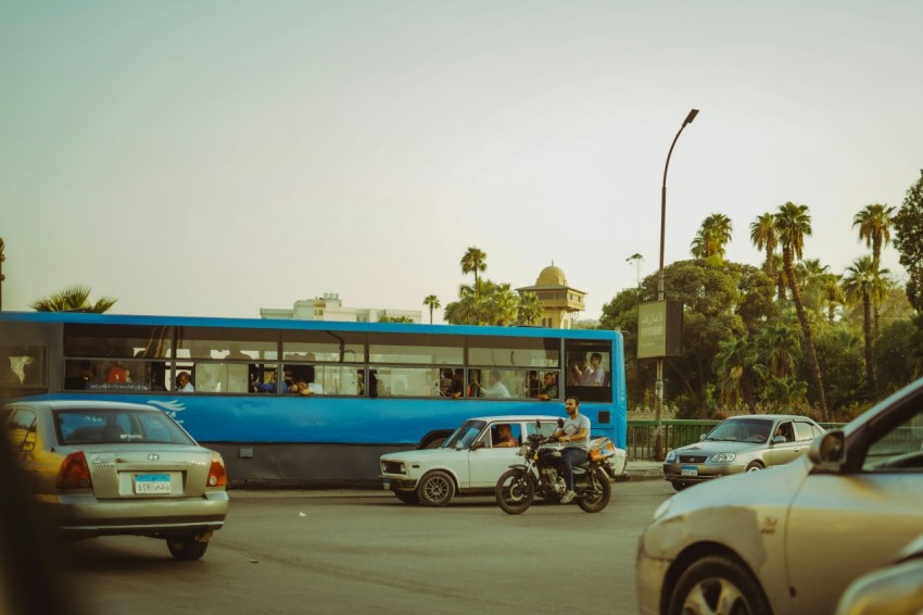 a blue bus driving down a street next to parked cars