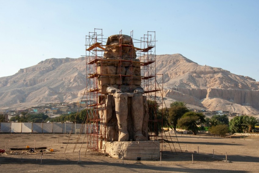 sitting egyptian statue on soil field near trees during day