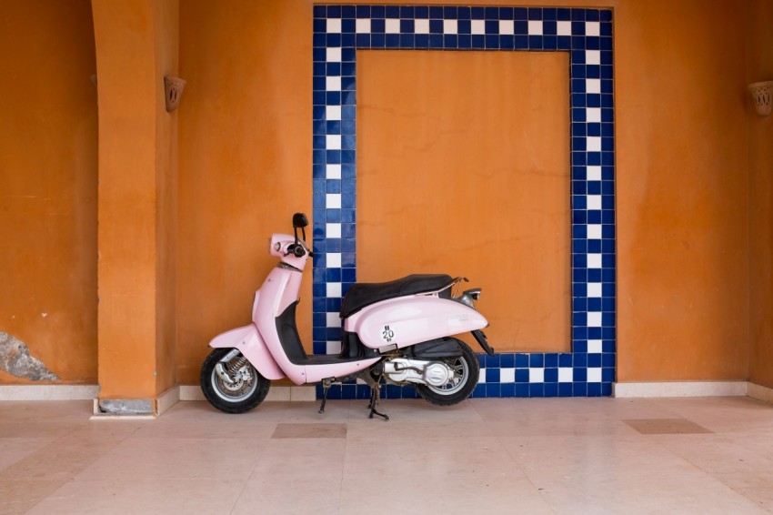 white and blue motor scooter parked beside orange and blue wall