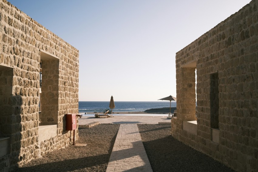 a stone building next to the ocean with a beach in the background Gk