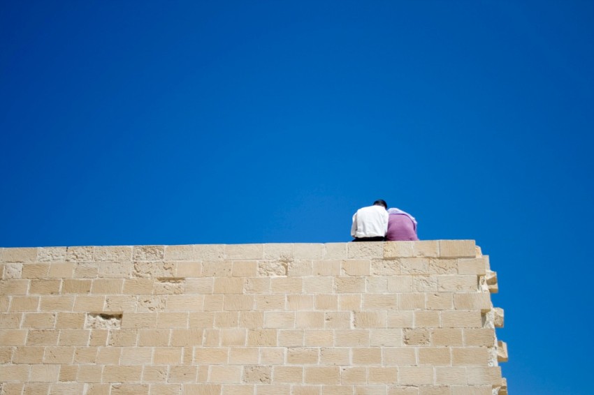 man in white shirt sitting on brown concrete wall during daytime