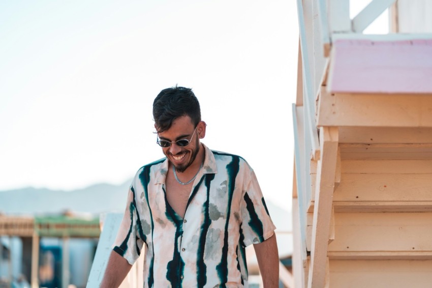 man in white green and black button up shirt standing near brown wooden fence during daytime