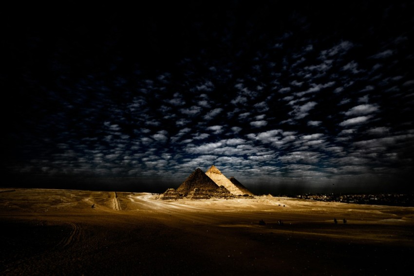 a pyramid in the middle of a desert under a cloudy sky