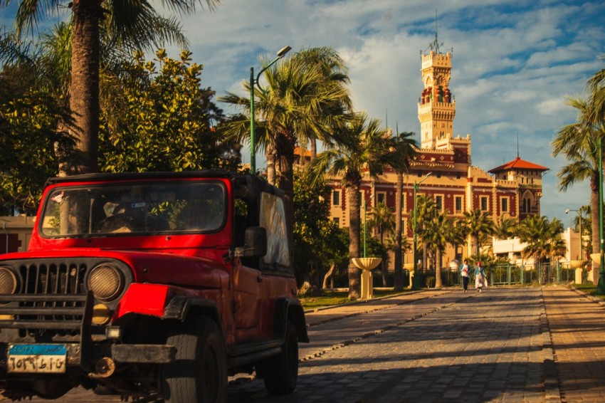 a red jeep driving down a street next to palm trees