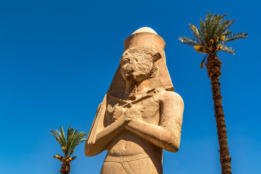 a statue of an egyptian woman with a palm tree in the background