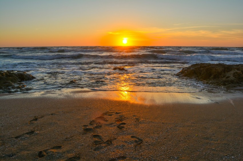 the sun is setting over the ocean with footprints in the sand