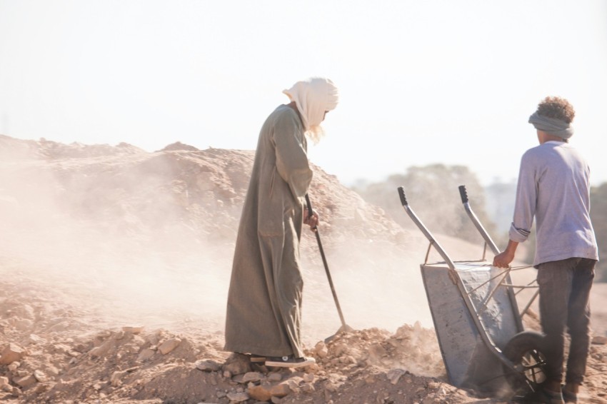 a man and a woman with a wheelbarrow on a dirt field