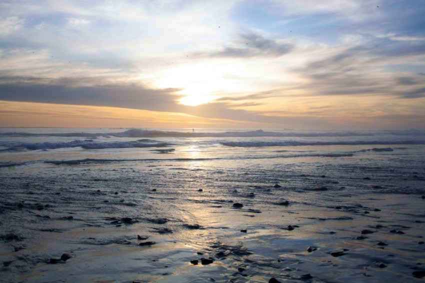 a beach with waves and the sun setting