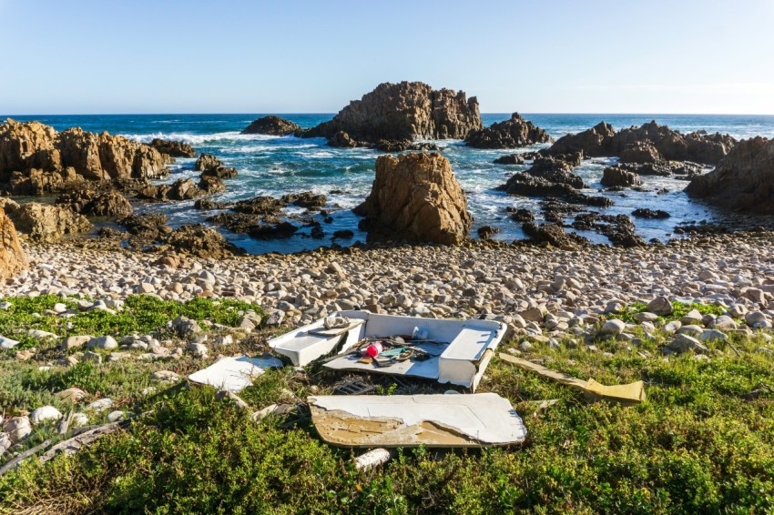 a couch sitting on top of a rocky beach next to the ocean CJ