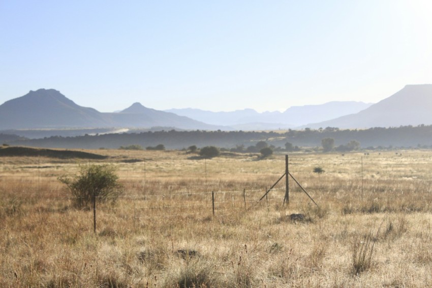 a field with a fence and mountains in the background