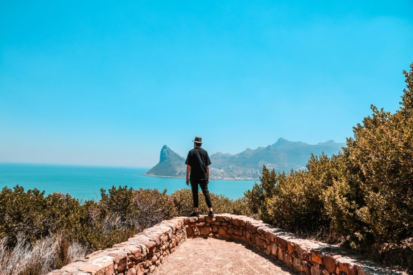 man in black jacket standing on brown concrete pathway near body of water during daytime