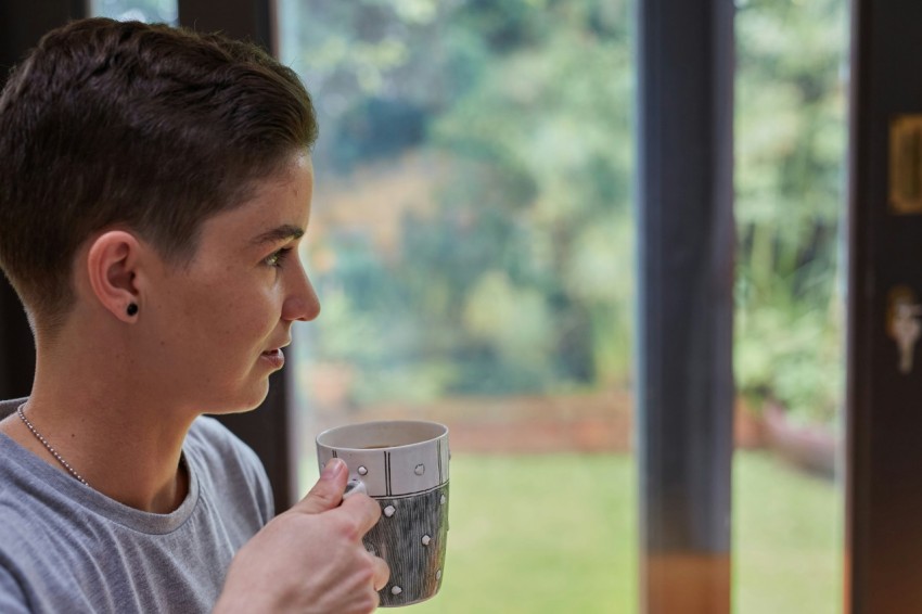 a person holding a cup looking out a window