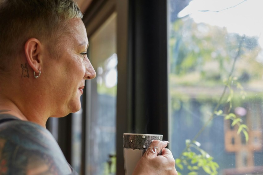 a person holding a cup looking out a window ZC