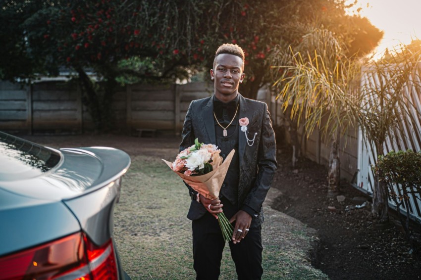 man on black coat and black bottoms holding white flower bouquet