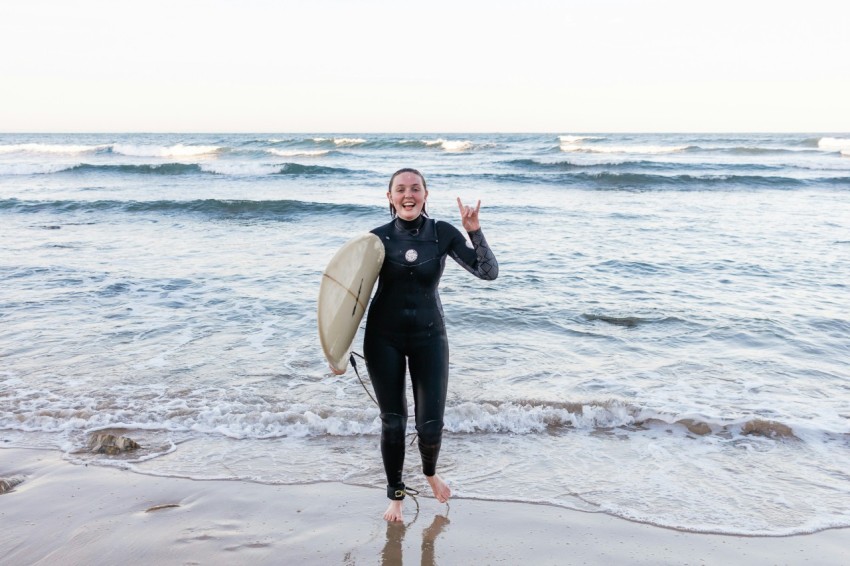 woman in black wetsuit holding white surfboard standing on beach during daytime