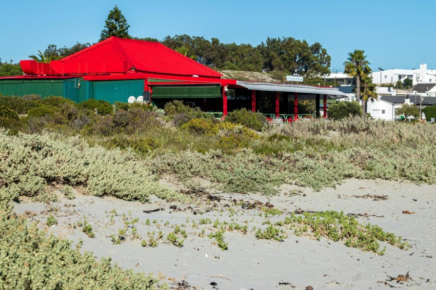 a red roofed building sitting on top of a sandy beach