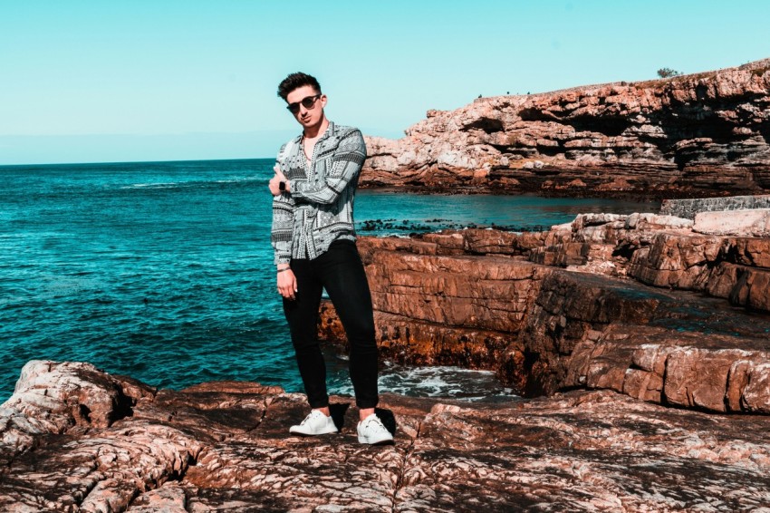 man in black pants standing on rock formation near body of water during daytime