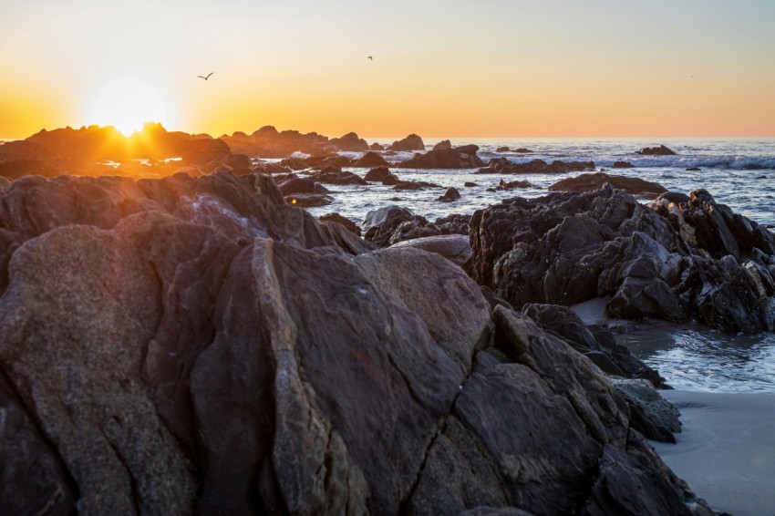 the sun is setting over the ocean and rocks