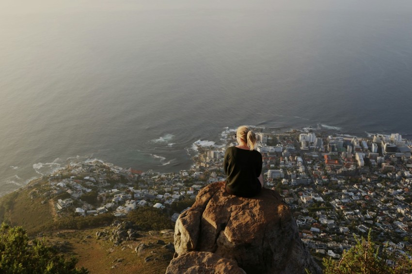 woman sitting on top of rocky mountain watching view of city