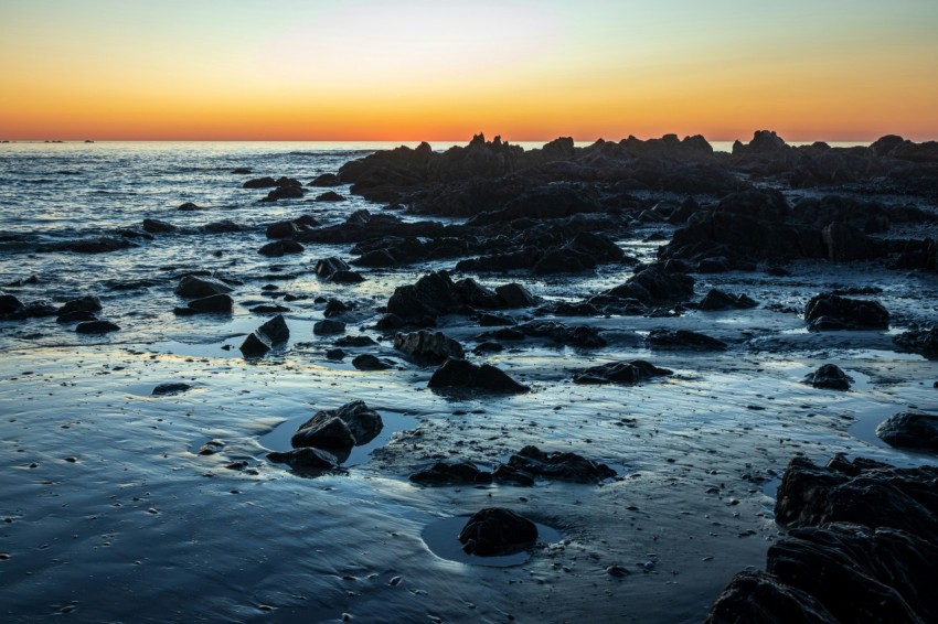 the sun is setting over a rocky beach