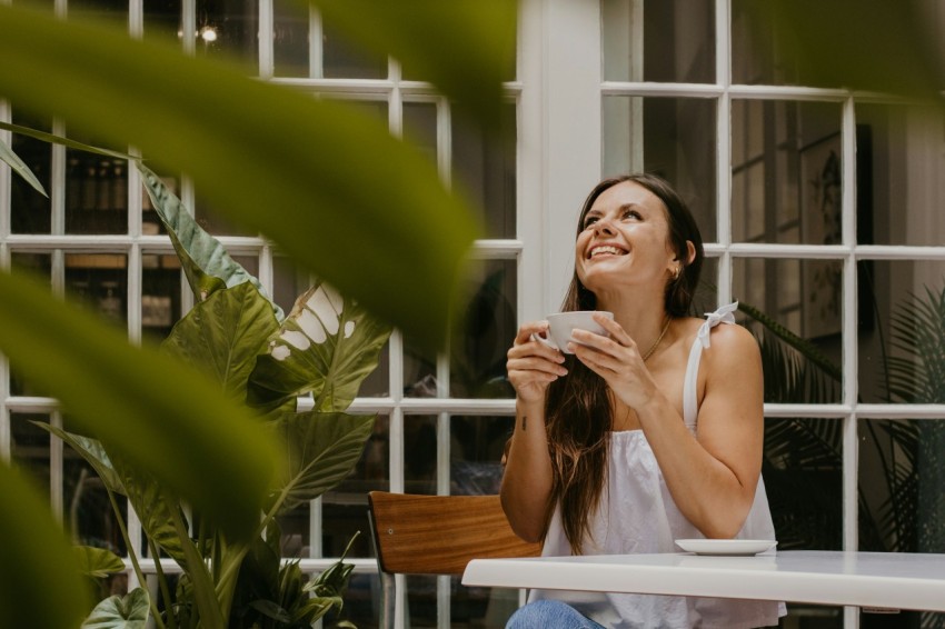 a woman sitting at a table drinking a cup of coffee 7w_aPSt