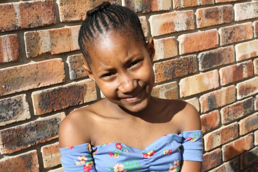 a young girl standing in front of a brick wall