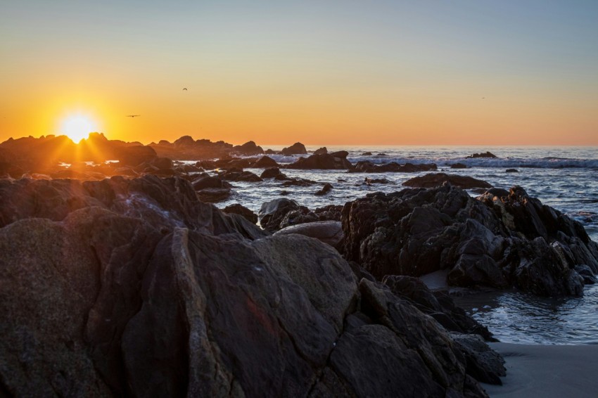 the sun is setting over the ocean and rocks