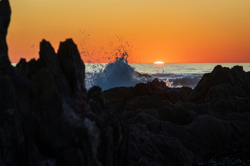 the sun is setting over the ocean and rocks